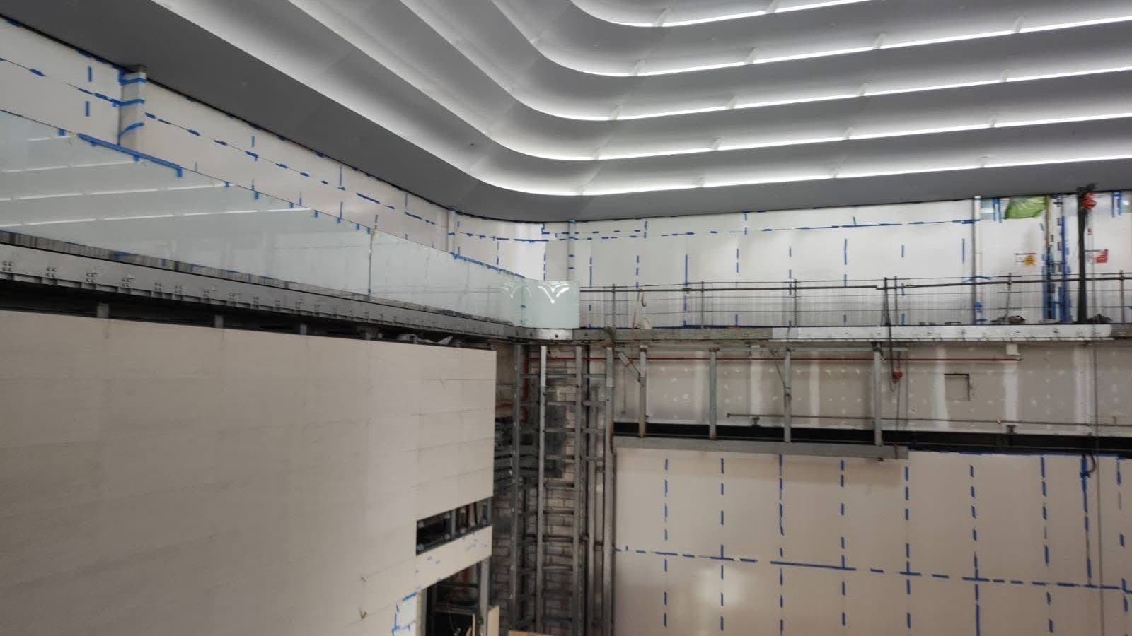 Curved gallery edge and lit ceiling ribs above stone cladding set-out