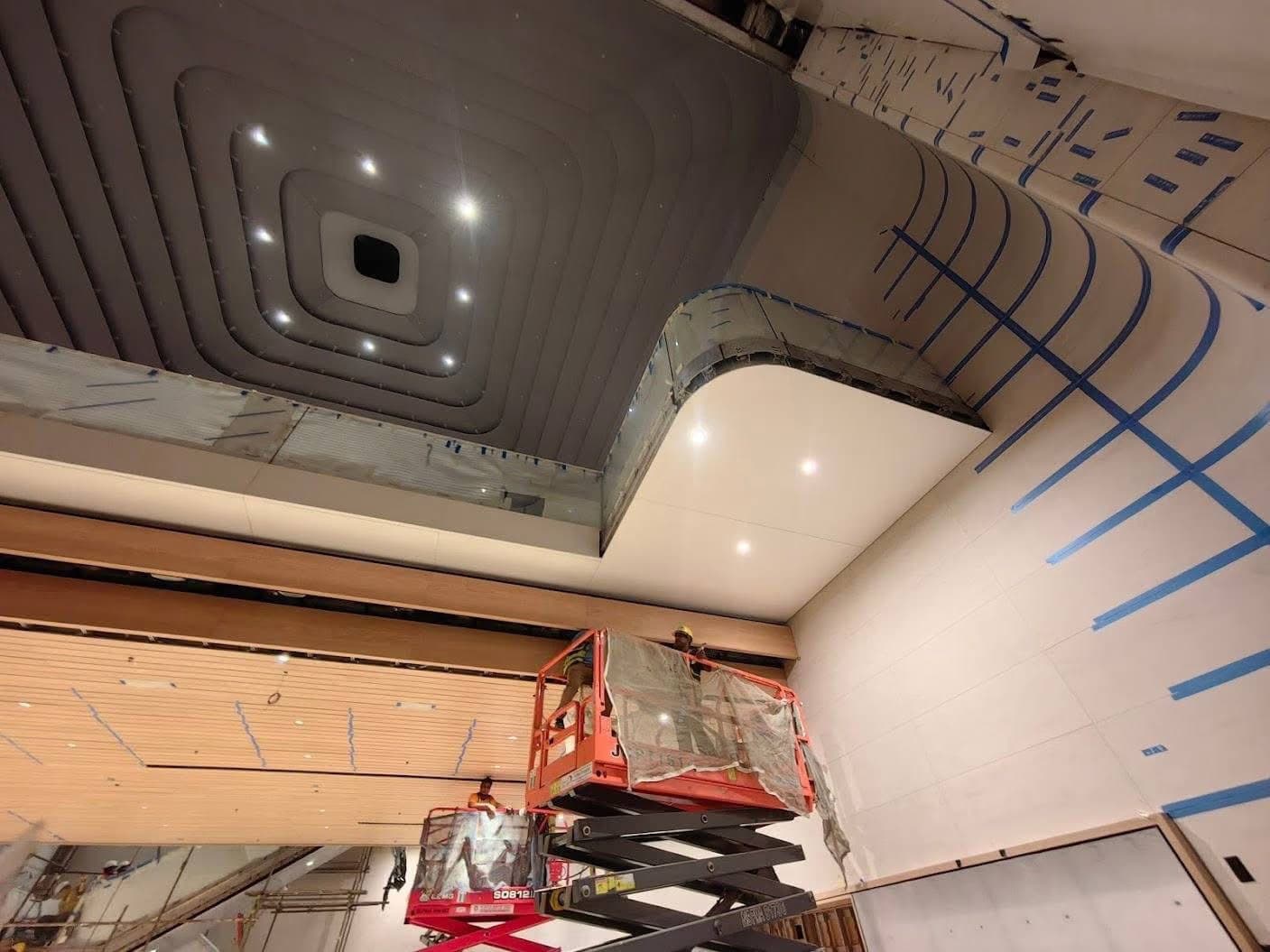 Installers on scissor lifts fixing curved soffit panels under the stepped ceiling